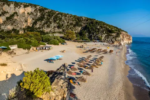 Słoneczne albania plaże z rzędami leżaków i parasoli, skaliste zbocze i turkusowe morze.