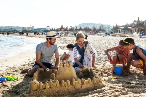 Rodzina buduje zamek z piasku na plaży, idealne miejsce na tunezja wycieczki. Dzieci bawią się z rodzicami, tworząc wspomnienia.