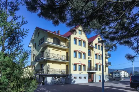 Hotel Milena w Milówce, żółty budynek z balkonami i czerwonym dachem, otoczony zielenią.