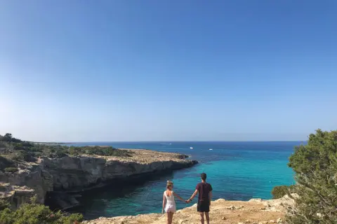 Para spaceruje po klifie, podziwiając turkusowe wody i skaliste wybrzeże Akamas.