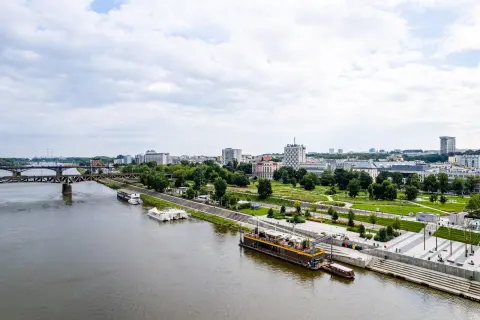 Widok na Wisłę i warszawskie Powiśle z nowoczesnymi bulwarami, mostem i zabudową miejską w tle.