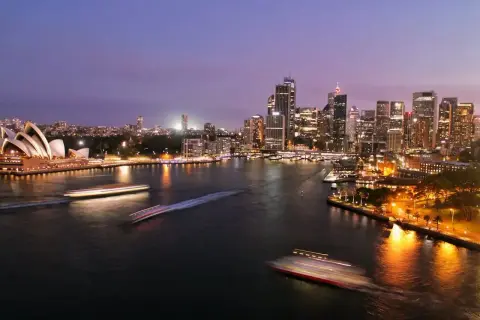 Sydney nocą, z Operą i drapaczami chmur. Zastanawiasz się, ile się leci do Australii?