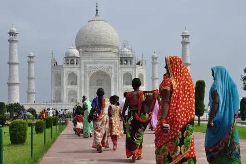 Kobiety w barwnych sari spacerują ścieżką ku Taj Mahal. Marzenie o podróży do Indii i uzyskaniu wizy do Indii staje się rzeczywistością.
