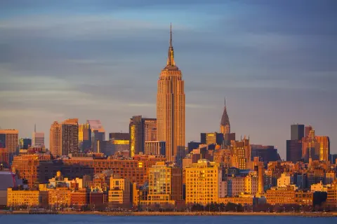 Zachód słońca nad Manhattanem. Widać Empire State Building i Chrysler Building. Zastanawiasz się, ile się leci do Nowego Jorku?