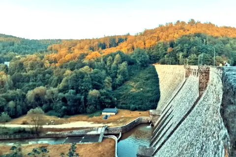 Kamienna zapora wodna w Zagórzu Śląskim otoczona zielonymi wzgórzami oświetlonymi zachodzącym słońcem.