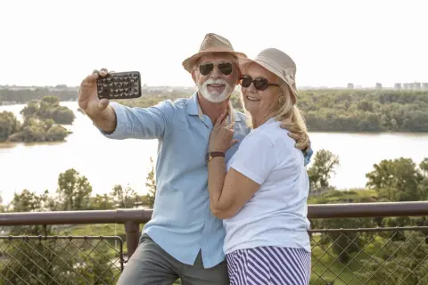 Szczęśliwa para seniorów robi selfie na tle rzeki i zieleni. Marzą o podróżach dla seniorów samolotem.
