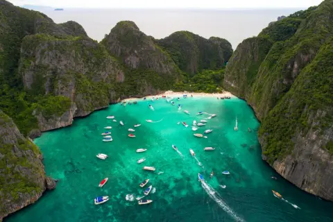 Maya Bay tętni życiem, pełna łodzi i turystów na piaszczystej plaży, otoczona stromymi, zielonymi klifami.
