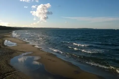Spokojna plaża Jelitkowo o zachodzie słońca. Woda faluje, a na piasku widać kałuże i mewy.
