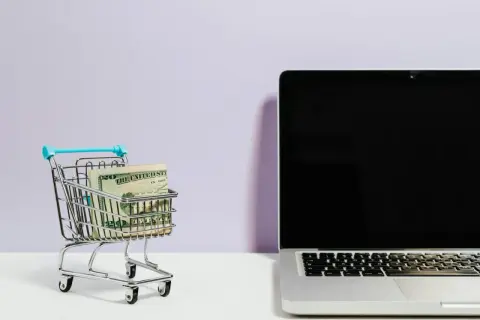 Mini wózek sklepowy z pieniędzmi obok laptopa. Idealne do szukania najlepszych reisen opinie i planowania podróży.