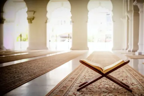 Otwarta księga na drewnianym stojaku w meczecie, symbolizująca turcja religia. Wnętrze z łukami i dywanami tworzy atmosferę spokoju.