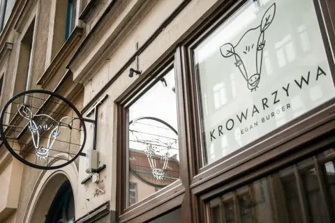 Neonowy znak i logo na szybie lokalu Krowarzywa. Wesoła krowa zaprasza na wegańskie burgery.