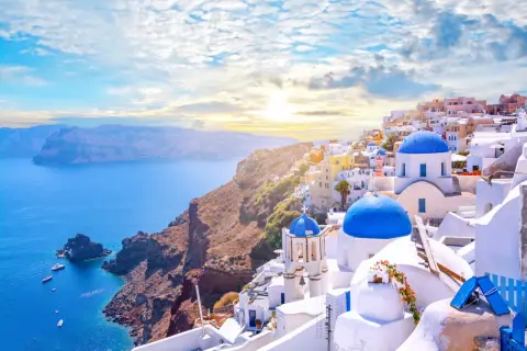 Widok na białe domy z niebieskimi dachami na Santorini, idealne miejsce na loty do Grecji. Morze i góry w tle.