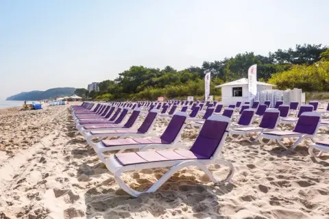 Idealne tanie wczasy nad morzem dla 2 osób z wyżywieniem. Rzędy leżaków na piaszczystej plaży, morze i zieleń w tle.