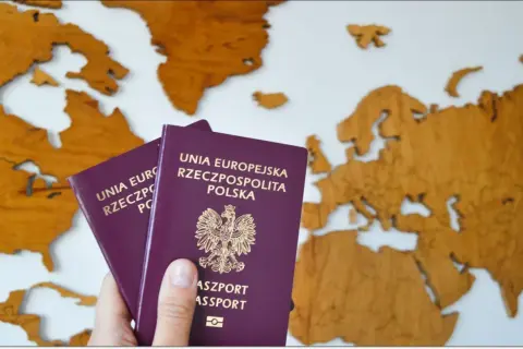 Dwa polskie paszporty, w tym paszport tymczasowy dla dziecka, na tle drewnianej mapy Europy.