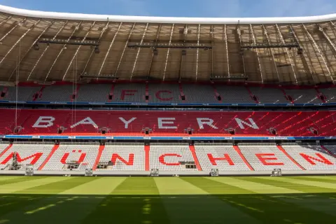 Puste trybuny Allianz Arena z napisem "BAYERN MÜNCHEN" w czerwonych i białych siedzeniach.