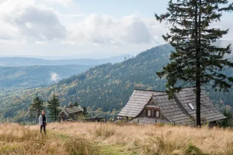 Widok na malownicze góry w Polsce. Drewniany domek i samotna turystka na tle jesiennych lasów i pagórków.