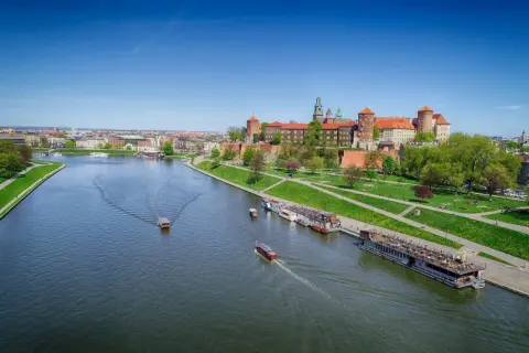 Widok na Wawel i rzekę Wisłę z łodziami. Słoneczny dzień zachęca do spacerów po zielonych bulwarach.