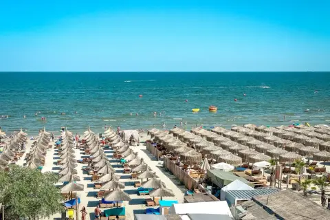 Słoneczny dzień na plaży nad Morzem Czarnym w Rumunii. Rzędy parasoli, ludzie kąpiący się i pływający.