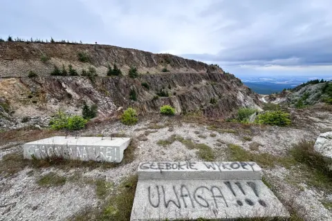 Krajobraz po kopalni kwarcu Stanisław. Na pierwszym planie betonowe płyty z napisami, w tle skalne zbocza i widok na dolinę.
