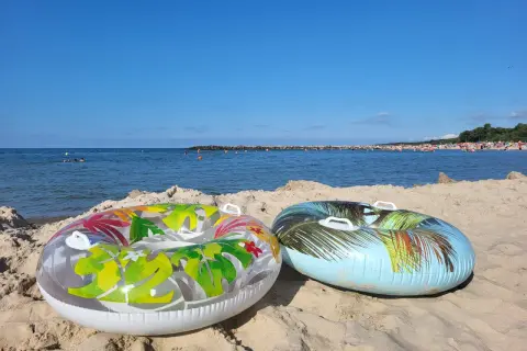 Dwa dmuchane koła na piaszczystej plaży, morze i tłumy ludzi w tle. Idealne na wakacje.pl opinie.