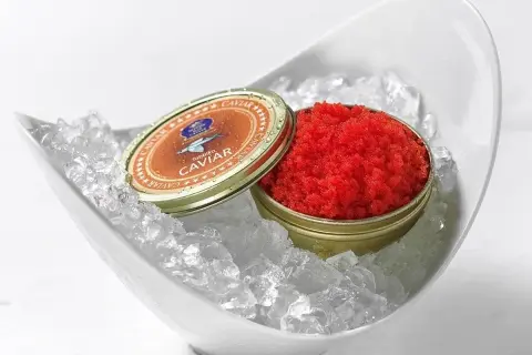 Czerwony kawior tobiko w puszce, podany na lodzie w białej misie.