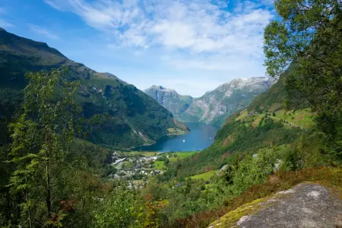 Widok na malownicze **Stavanger fiordy** z zielonymi zboczami gór, błękitną wodą i małym miasteczkiem u podnóża.