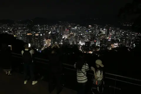 Nocny widok na rozświetlone miasto, przypominające panoramę Gangnam. Ludzie robią zdjęcia, podziwiając miejski krajobraz.
