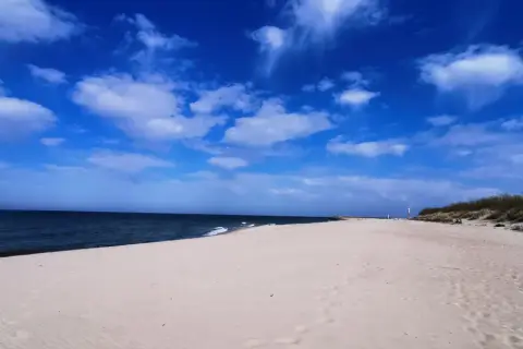 Piękna, słoneczna pogoda na sierpień nad morzem. Szeroka, piaszczysta plaża, spokojne morze i błękitne niebo z białymi chmurami.