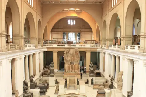 Wielka sala w muzeum w Kairze, pełna starożytnych posągów i artefaktów. Monumentalne rzeźby faraonów dominują w centrum.