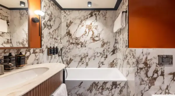 Łazienka w Mercure Gdynia Centrum. Marmurowe ściany, wanna, umywalka i pomarańczowe akcenty. Opinie o hotelu często podkreślają jego nowoczesny design.