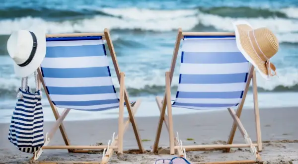 Dwie leżaki na plaży, gotowe na wakacje nad Bałtykiem. W tle morze i niebo.
