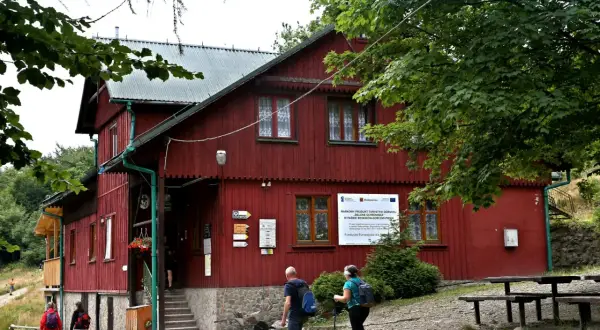 Schronisko PTTK Leskowiec, czerwony budynek w górach, turyści zbliżają się do wejścia.