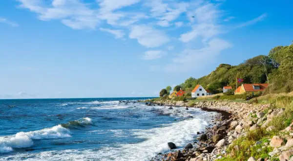 Kamienista plaża i domki na wzgórzu tworzą malowniczy krajobraz. To urokliwa wyspa na Bałtyku, gdzie fale rozbijają się o brzeg.