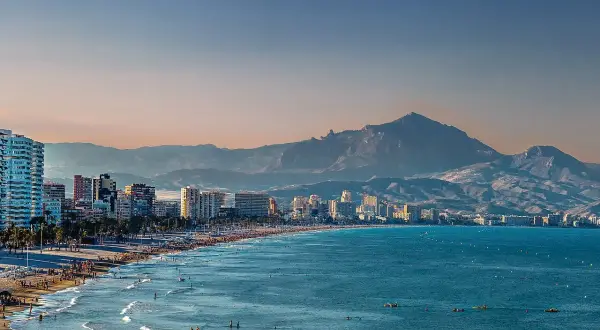 Alicante w grudniu: słoneczna plaża pełna ludzi, turkusowe morze i góry w tle. Idealna pogoda na spacer.