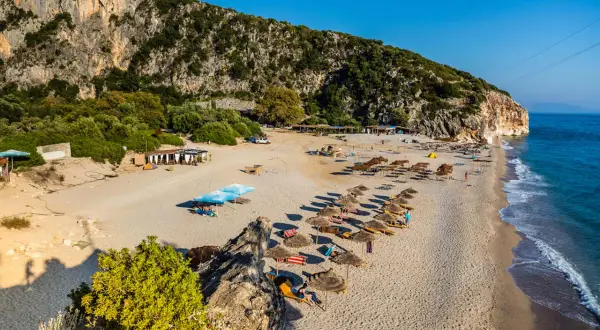 Słoneczne albania plaże z rzędami leżaków i parasoli, skaliste zbocze i turkusowe morze.
