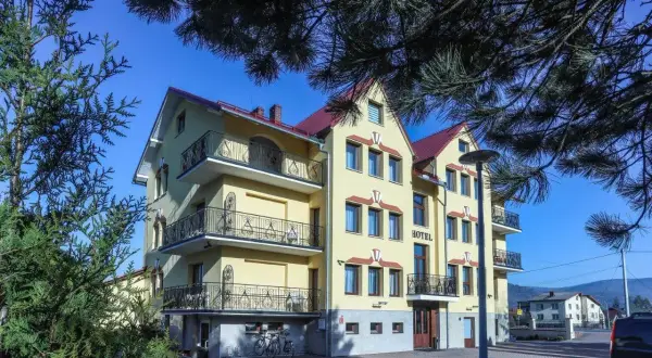 Hotel Milena w Milówce, żółty budynek z balkonami i czerwonym dachem, otoczony zielenią.