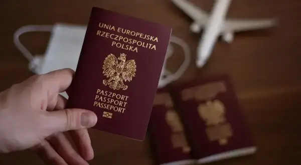 Dłoń trzyma polski paszport. Obok leżą kolejne paszporty, maseczka i samolot, sugerując podróż i pytając, ile wyrabia się paszport.