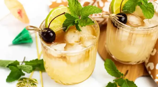 Dwa orzeźwiające drinki Mai Tai z lodem, limonką, wiśnią i miętą, ozdobione parasolkami.