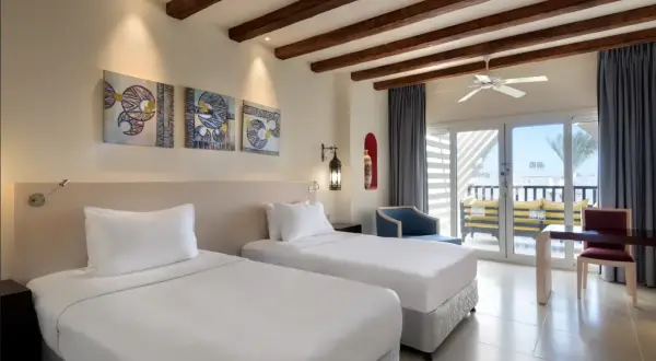 Pokój w Hilton Marsa Alam Nubian Resort. Dwa białe łóżka, obrazy w stylu nubijskim, balkon z widokiem na morze.