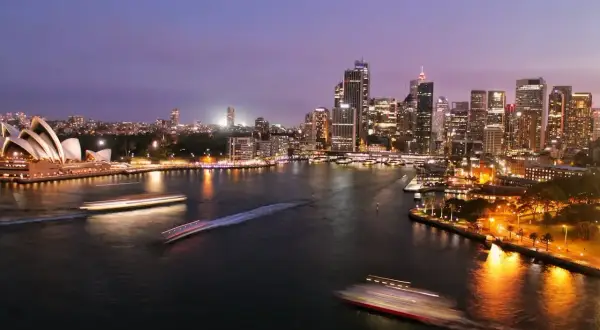 Sydney nocą, z Operą i drapaczami chmur. Zastanawiasz się, ile się leci do Australii?