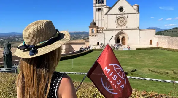 Kobieta w kapeluszu z flagą Misja Travel przed bazyliką. Wspaniałe widoki i pozytywne misja travel opinie.