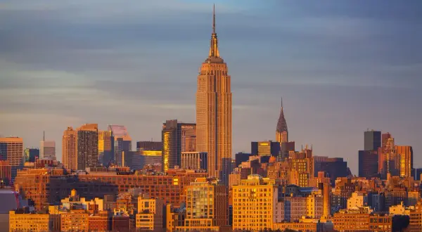 Zachód słońca nad Manhattanem. Widać Empire State Building i Chrysler Building. Zastanawiasz się, ile się leci do Nowego Jorku?
