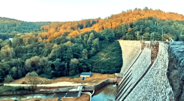 Kamienna zapora wodna w Zagórzu Śląskim otoczona zielonymi wzgórzami oświetlonymi zachodzącym słońcem.