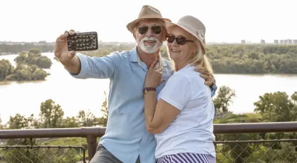Szczęśliwa para seniorów robi selfie na tle rzeki i zieleni. Marzą o podróżach dla seniorów samolotem.