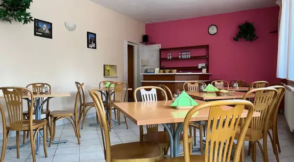Wnętrze restauracji z drewnianymi stołami i krzesłami, różową ścianą i zielonymi roślinami.