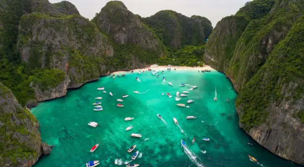 Maya Bay tętni życiem, pełna łodzi i turystów na piaszczystej plaży, otoczona stromymi, zielonymi klifami.