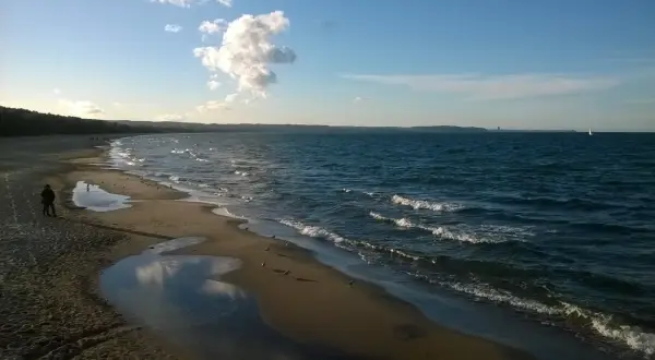 Spokojna plaża Jelitkowo o zachodzie słońca. Woda faluje, a na piasku widać kałuże i mewy.