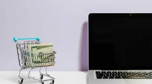 Mini wózek sklepowy z pieniędzmi obok laptopa. Idealne do szukania najlepszych reisen opinie i planowania podróży.