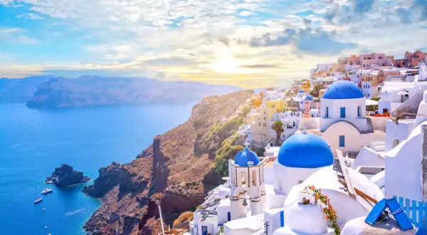 Widok na białe domy z niebieskimi dachami na Santorini, idealne miejsce na loty do Grecji. Morze i góry w tle.