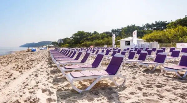 Idealne tanie wczasy nad morzem dla 2 osób z wyżywieniem. Rzędy leżaków na piaszczystej plaży, morze i zieleń w tle.
